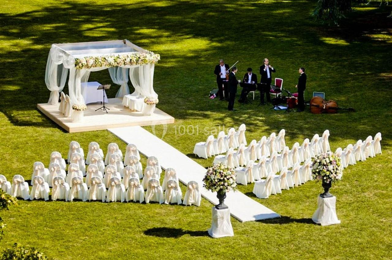 Cérémonie de mariage en plein air avec une allée centrale, une arche décorée et un quatuor jouant en arrière-plan.