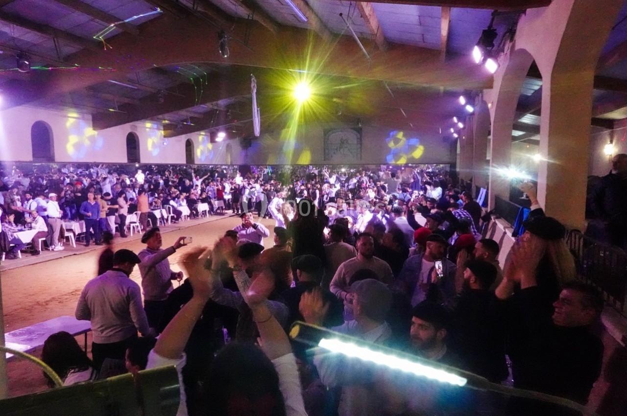 Salle comble avec des spectateurs applaudissant lors d’un événement festif sous un éclairage coloré.