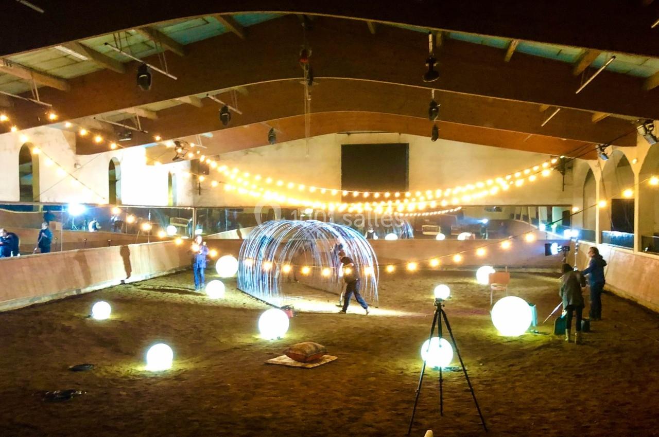 Manège équestre décoré de guirlandes lumineuses et de sphères éclairées, avec des structures métalliques au centre.