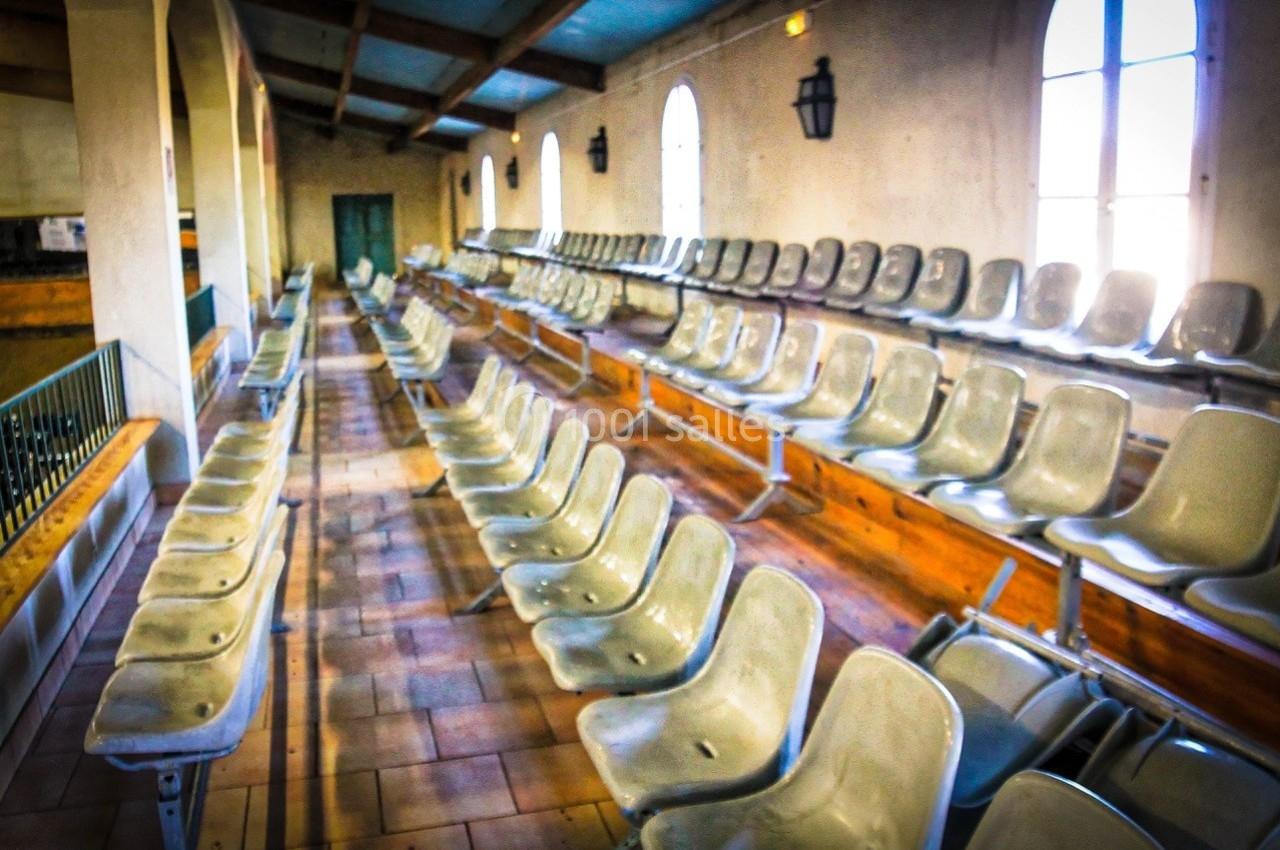 Rangées de sièges en plastique beige dans une salle avec des murs clairs et des fenêtres arquées.