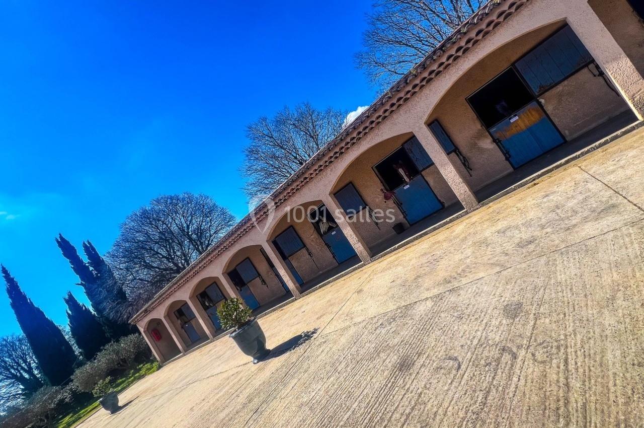 Alignement de boxes équestres en pierre avec portes bleues, entourés d'arbres sous un ciel bleu dégagé.