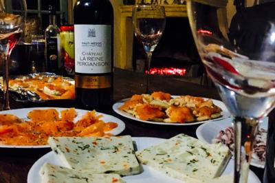 Assortiment de fromages et saumon fumé sur une table avec une bouteille de vin rouge, verres et cheminée en arrière-plan.