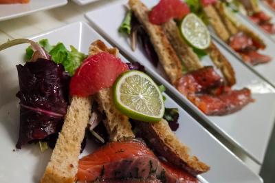 Assortiment de fromages et saumon fumé sur une table avec une bouteille de vin rouge, verres et cheminée en arrière-plan.