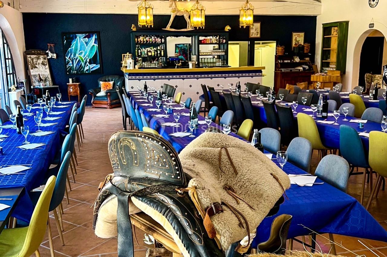 Salle de restaurant décorée avec des tables dressées en bleu, un bar en arrière-plan et une selle exposée au premier plan.