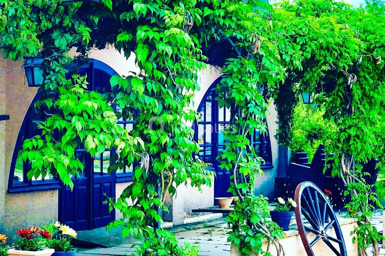Façade d'un restaurant avec des arches couvertes de végétation et une roue en bois décorative au premier plan.