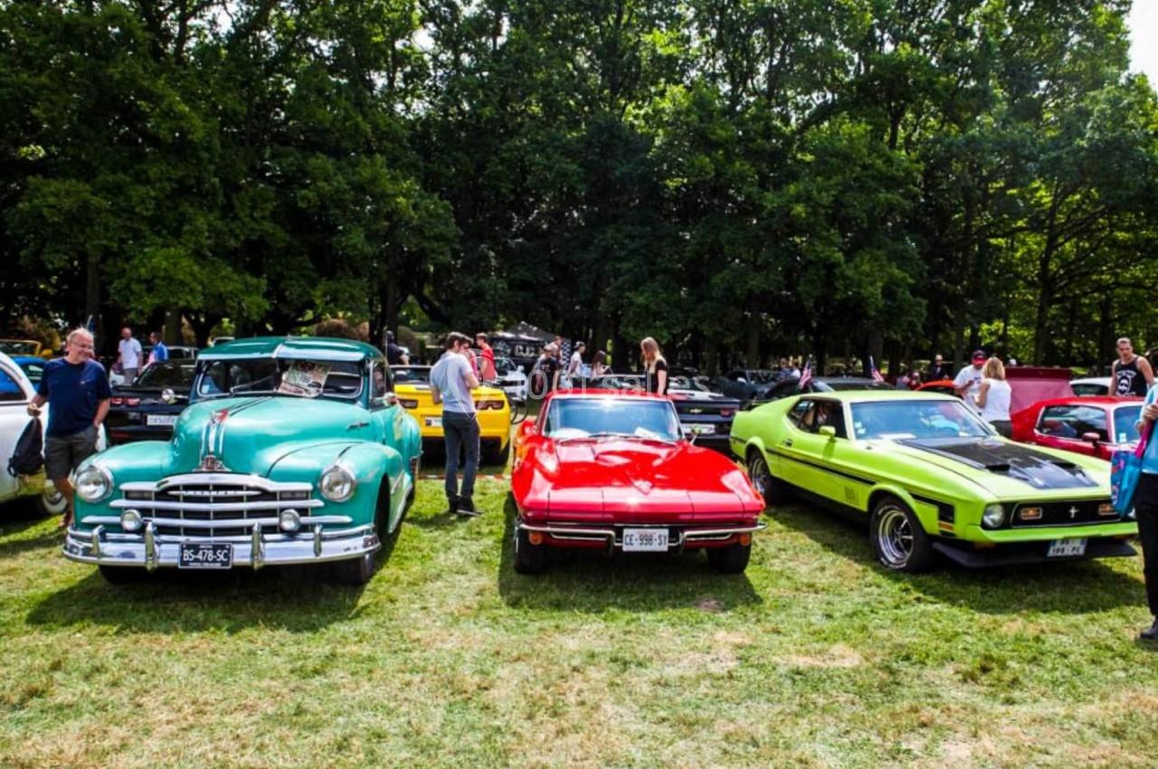 Des voitures anciennes et de collection exposées sur une pelouse, entourées de visiteurs et d'arbres en arrière-plan.