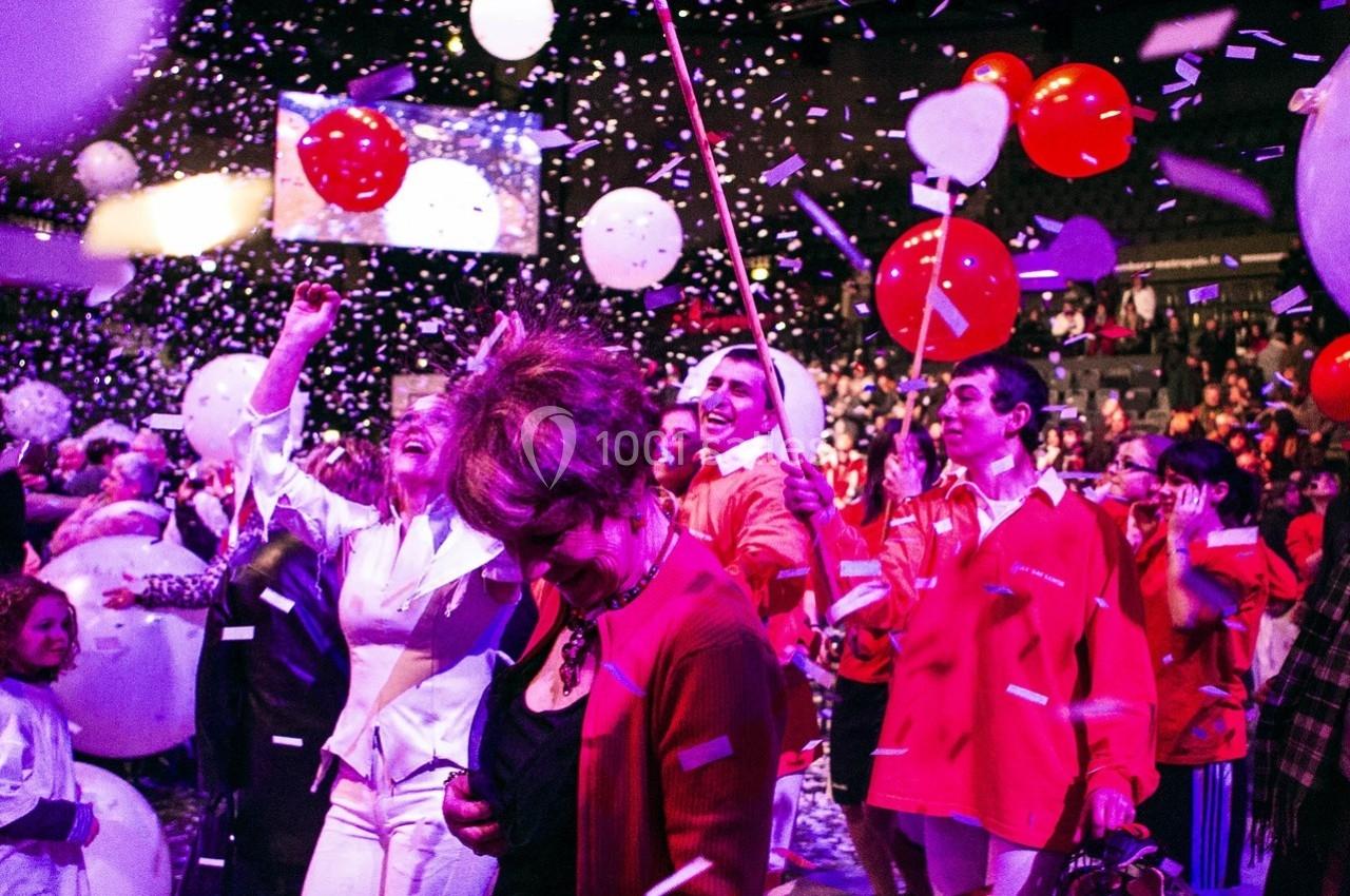 Des personnes en liesse dans une salle festive, entourées de confettis, ballons rouges et blancs.