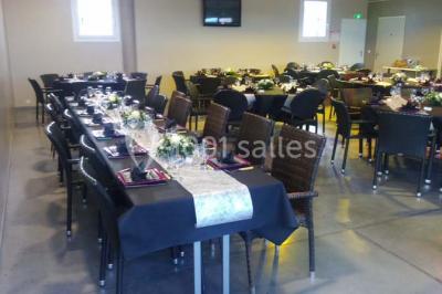 Table ronde dressée avec des verres, couverts et serviettes vertes, entourée de chaises, avec un buffet en arrière-plan.