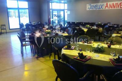 Table ronde dressée avec des verres, couverts et serviettes vertes, entourée de chaises, avec un buffet en arrière-plan.