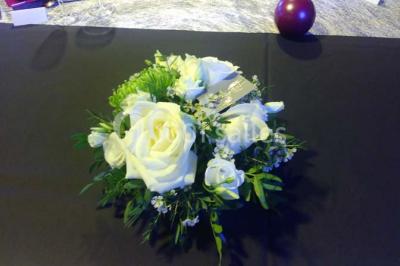 Table ronde dressée avec des verres, couverts et serviettes vertes, entourée de chaises, avec un buffet en arrière-plan.