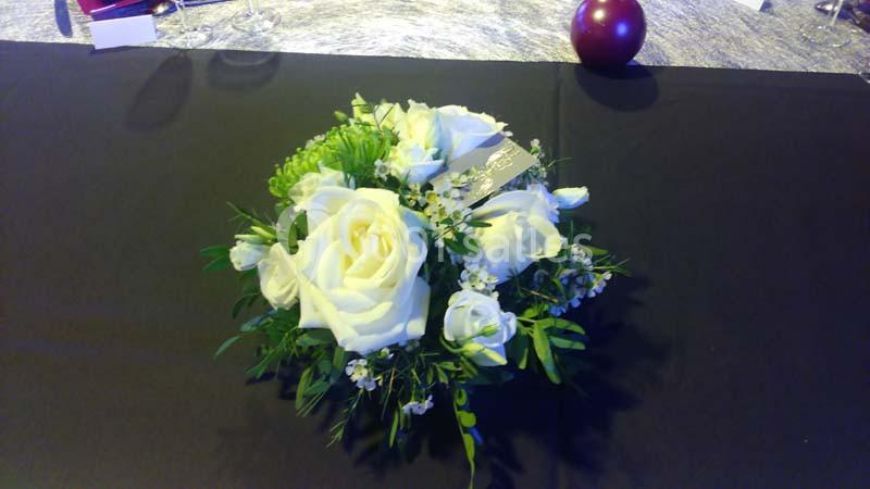 Centre de table avec des roses blanches et des feuillages verts sur une nappe noire.