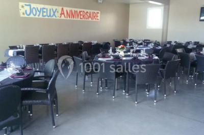 Table ronde dressée avec des verres, couverts et serviettes vertes, entourée de chaises, avec un buffet en arrière-plan.