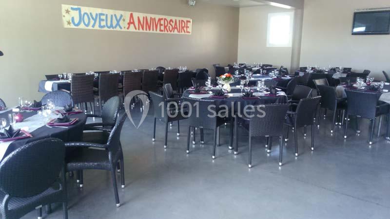 Salle décorée pour un anniversaire avec des tables dressées, nappes noires et une banderole ’Joyeux Anniversaire’ accrochée…