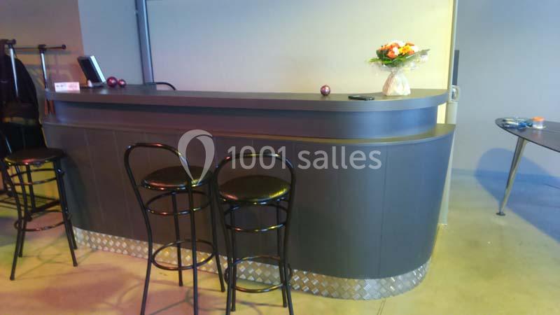 Comptoir de bar sombre avec trois tabourets noirs, un bouquet de fleurs et quelques objets posés dessus.