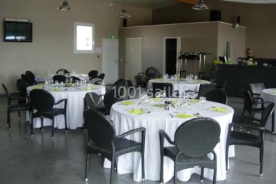 Table ronde dressée avec des verres, couverts et serviettes vertes, entourée de chaises, avec un buffet en arrière-plan.