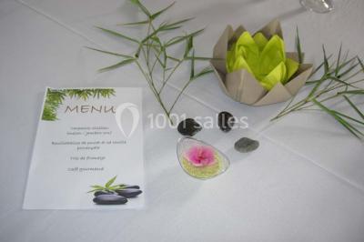 Table ronde dressée avec des verres, couverts et serviettes vertes, entourée de chaises, avec un buffet en arrière-plan.