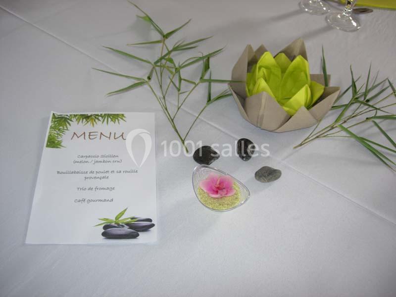 Menu imprimé posé sur une table blanche, décorée de bambous, galets, une fleur rose et une serviette pliée.