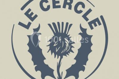 Table ronde dressée avec des verres, couverts et serviettes vertes, entourée de chaises, avec un buffet en arrière-plan.