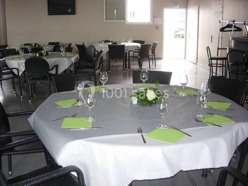 Salle de réception avec tables rondes dressées, nappes blanches, serviettes vertes et décoration florale.