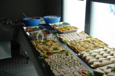 Table ronde dressée avec des verres, couverts et serviettes vertes, entourée de chaises, avec un buffet en arrière-plan.