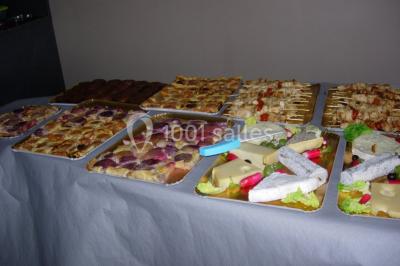 Table ronde dressée avec des verres, couverts et serviettes vertes, entourée de chaises, avec un buffet en arrière-plan.