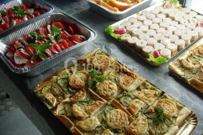 Table ronde dressée avec des verres, couverts et serviettes vertes, entourée de chaises, avec un buffet en arrière-plan.