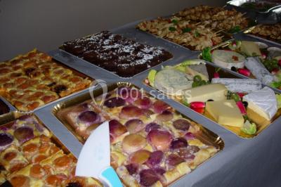 Table ronde dressée avec des verres, couverts et serviettes vertes, entourée de chaises, avec un buffet en arrière-plan.