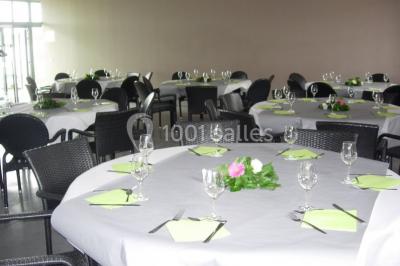 Table ronde dressée avec des verres, couverts et serviettes vertes, entourée de chaises, avec un buffet en arrière-plan.