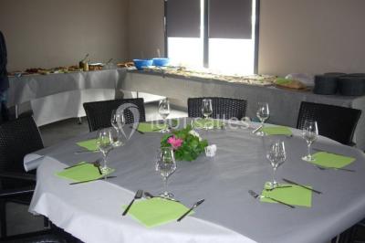 Table ronde dressée avec des verres, couverts et serviettes vertes, entourée de chaises, avec un buffet en arrière-plan.