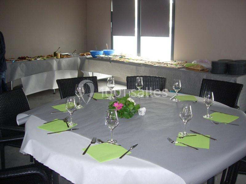 Table ronde dressée avec des verres, couverts et serviettes vertes, entourée de chaises, avec un buffet en arrière-plan.