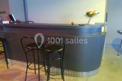 Salle avec des tables rondes dressées, nappes blanches, serviettes vertes, verres et décorations florales.