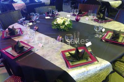 Salle avec des tables rondes dressées, nappes blanches, serviettes vertes, verres et décorations florales.