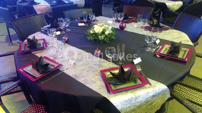 Table dressée avec nappes noires et grises, serviettes pliées en éventail, vaisselle élégante et centre de table floral.