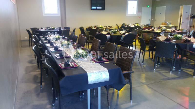 Salle décorée avec des tables alignées, nappes noires, chemins de table clairs et bouquets de fleurs.