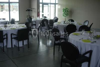 Salle avec des tables rondes dressées, nappes blanches, serviettes vertes, verres et décorations florales.