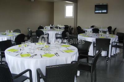 Salle avec des tables rondes dressées, nappes blanches, serviettes vertes, verres et décorations florales.