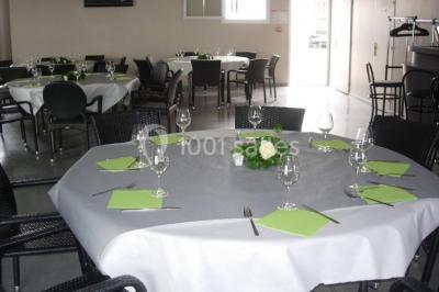 Salle avec des tables rondes dressées, nappes blanches, serviettes vertes, verres et décorations florales.
