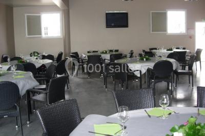 Salle avec des tables rondes dressées, nappes blanches, serviettes vertes, verres et décorations florales.