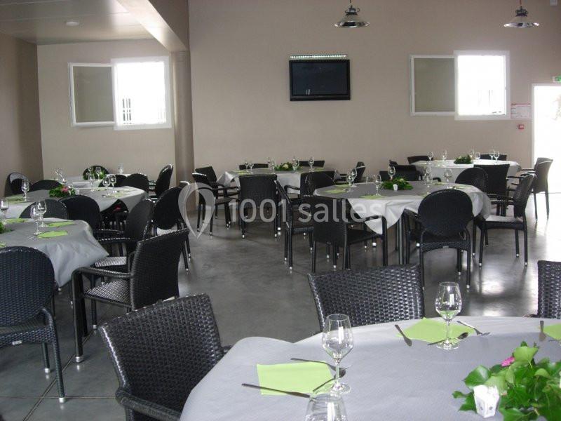 Salle de réception avec tables rondes dressées, nappes blanches, chaises noires et décorations vertes.