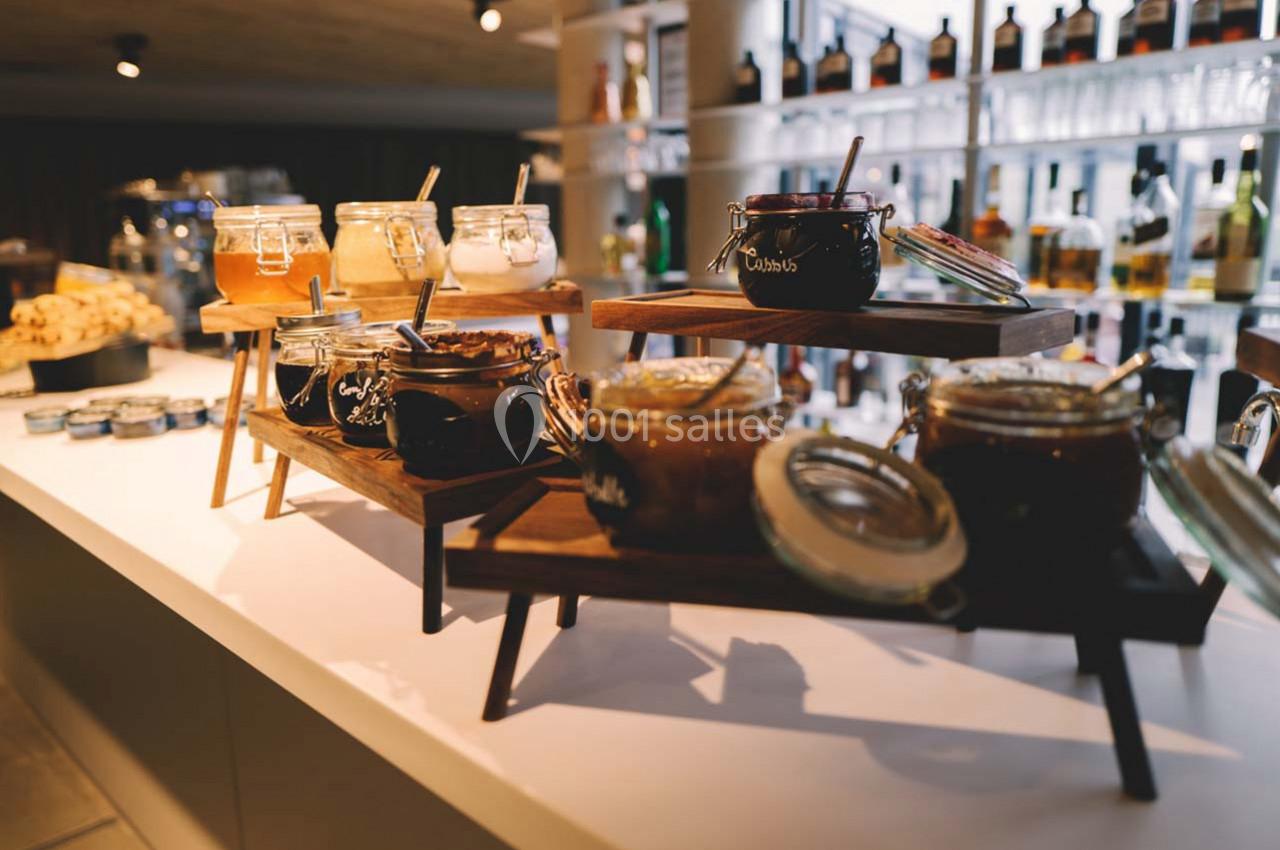 Pots de confitures variées disposés sur des étagères en bois dans un espace lumineux.