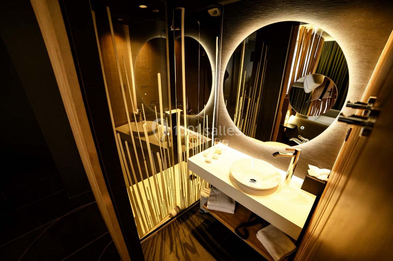Salle de bain moderne avec lavabo rond, miroir éclairé et paroi de douche ornée de motifs verticaux.