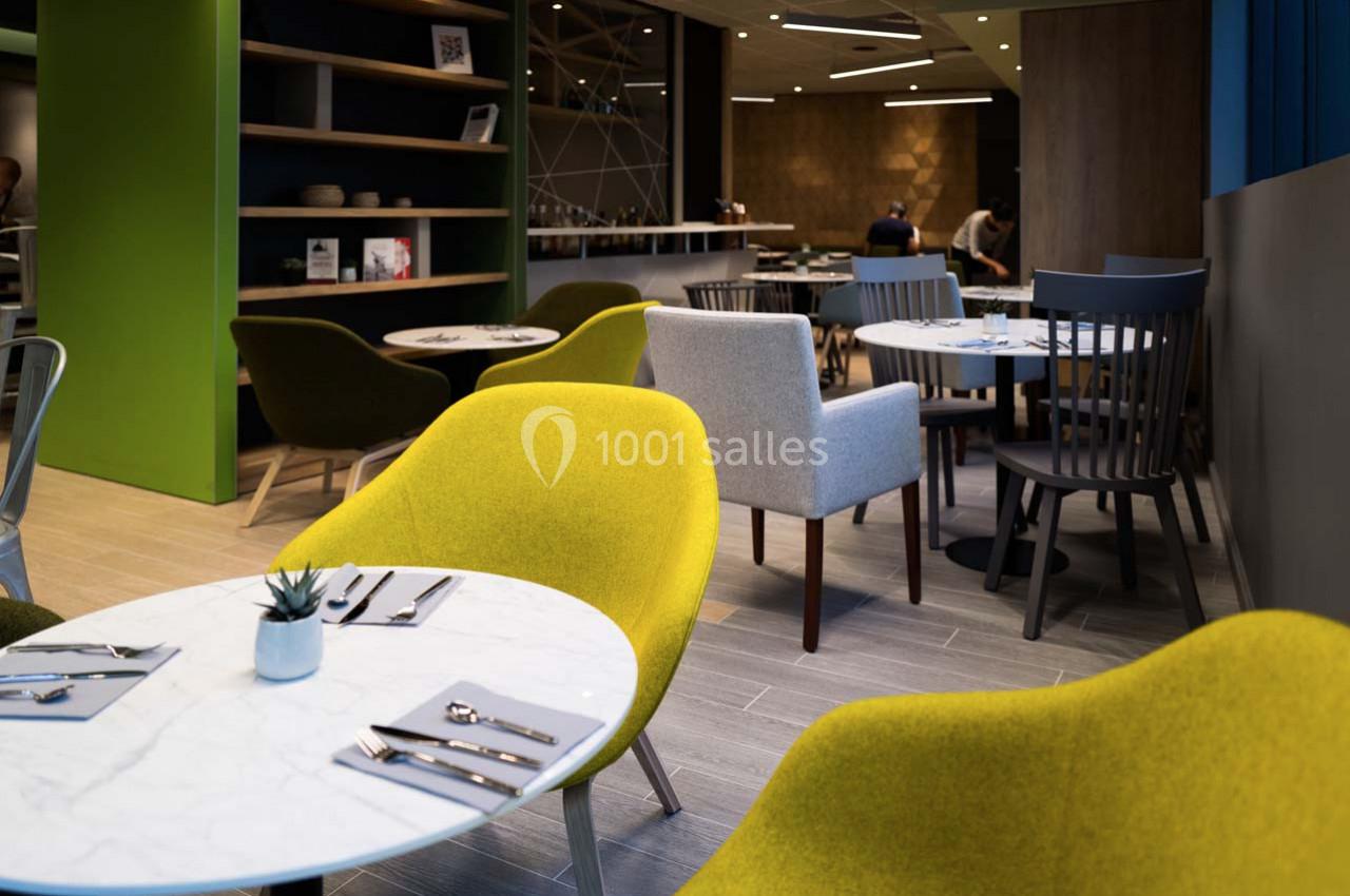 Salle de restaurant moderne avec tables rondes, chaises colorées et décoration épurée.