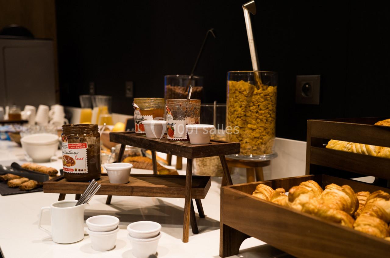 Buffet de petit-déjeuner avec croissants, céréales, confitures et boissons disposés sur une table.
