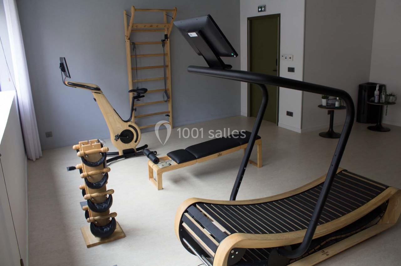 Salle de sport équipée d'un tapis de course en bois, d'un vélo d'exercice, d'haltères et d'un espalier.
