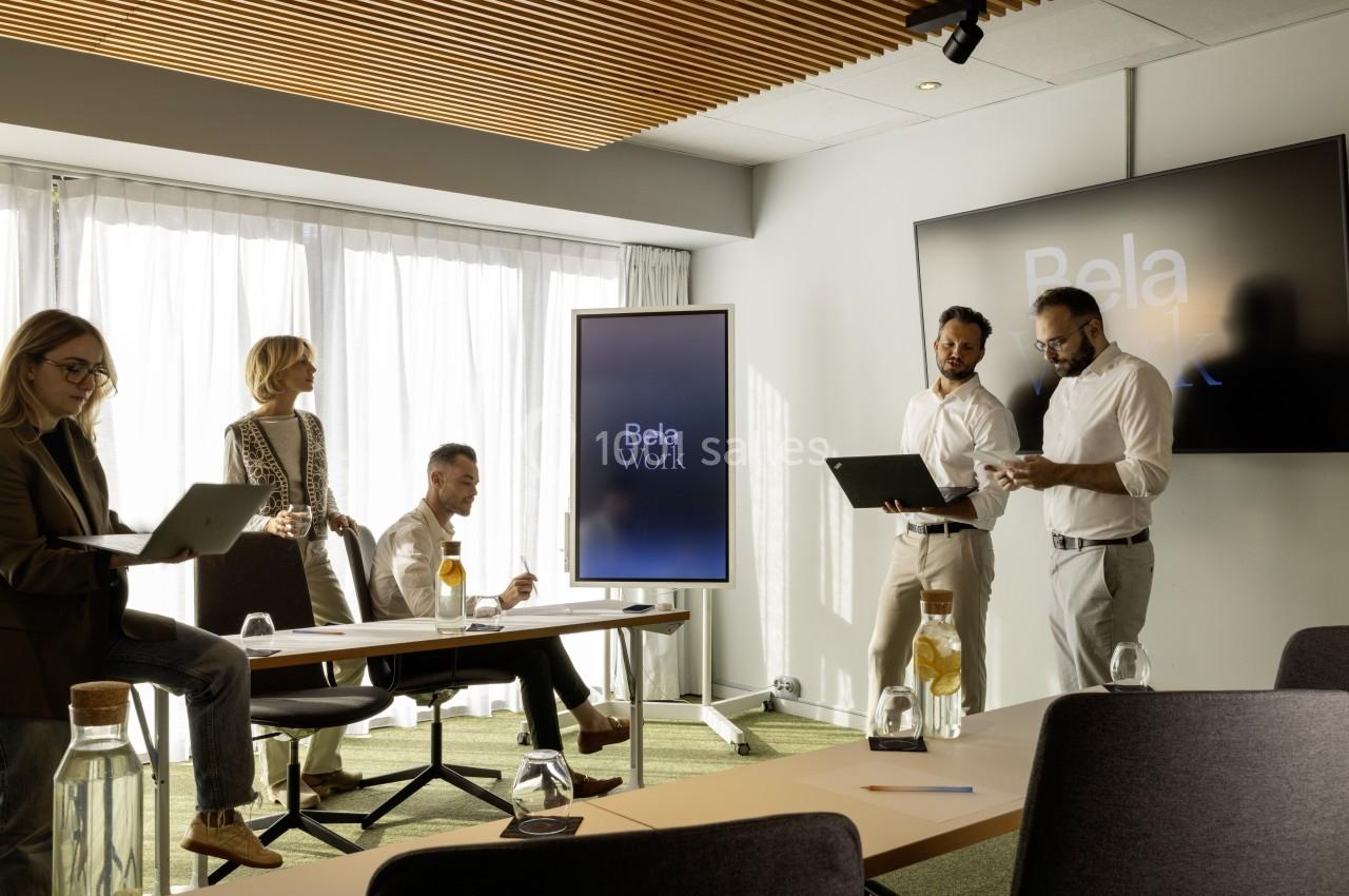 Un groupe de personnes travaille dans une salle de réunion lumineuse avec des écrans affichant ’Bela Work’.