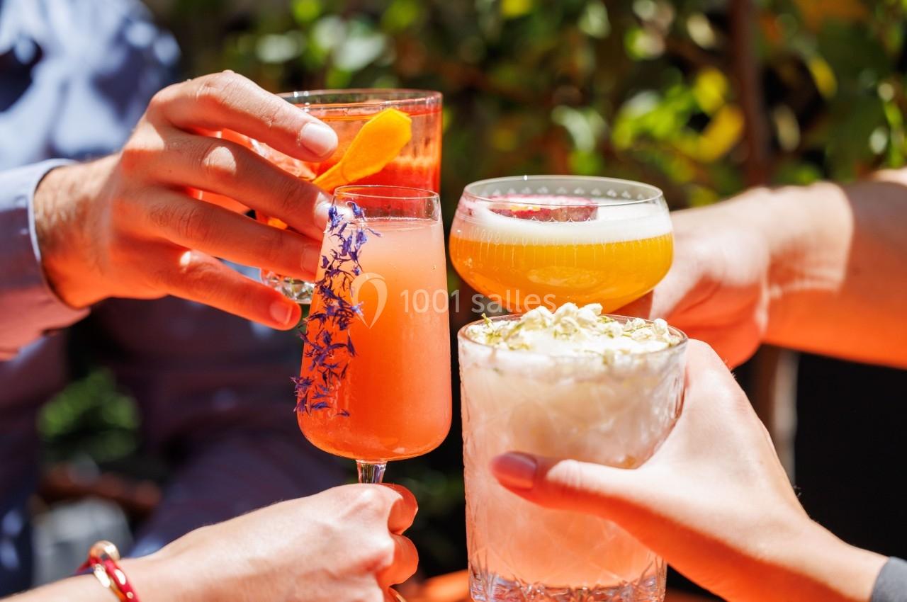 Quatre personnes trinquent avec des cocktails colorés dans un cadre extérieur ensoleillé.