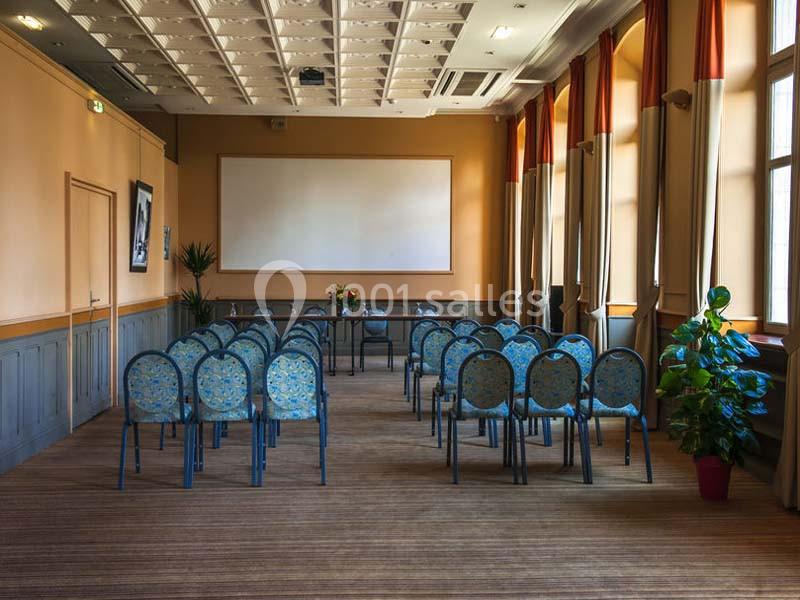 Salle de réunion lumineuse avec des rangées de chaises bleues, un tableau blanc et des plantes décoratives.