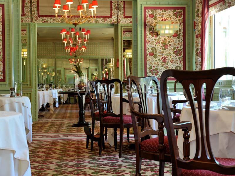 Location salle Divonne-les-Bains (Ain) - Domaine de Divonne #20 Salle de restaurant élégante avec tables dressées, chaises en bois sculpté et décor floral sur les murs et le sol.