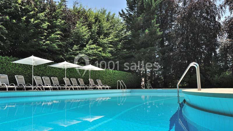 Location salle Divonne-les-Bains (Ain) - Domaine de Divonne #17 Piscine extérieure entourée de chaises longues, parasols blancs et haies verdoyantes sous un ciel dégagé.