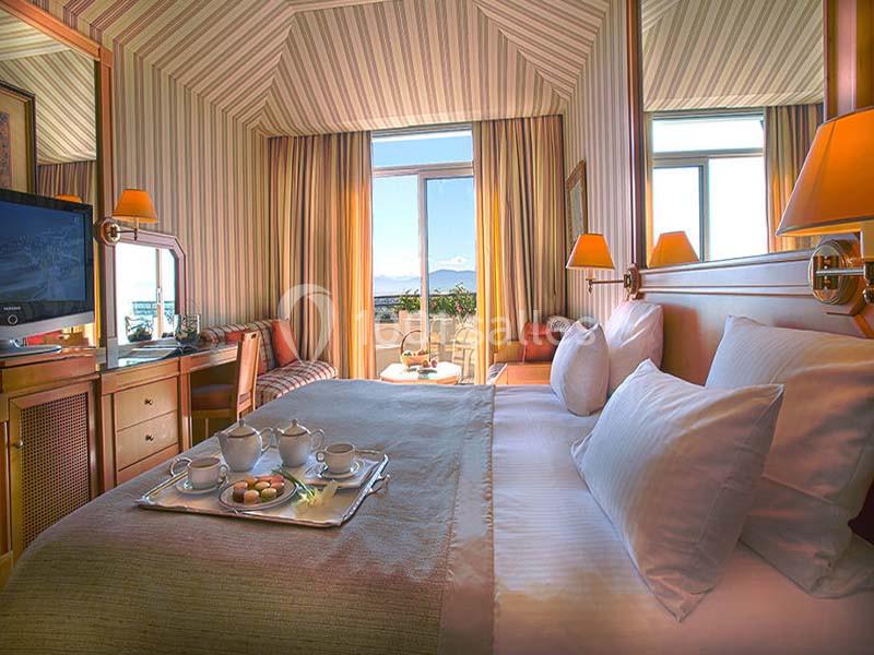 Location salle Divonne-les-Bains (Ain) - Domaine de Divonne #13 Chambre d'hôtel lumineuse avec lit double, plateau de thé, bureau, téléviseur et vue sur un paysage extérieur.